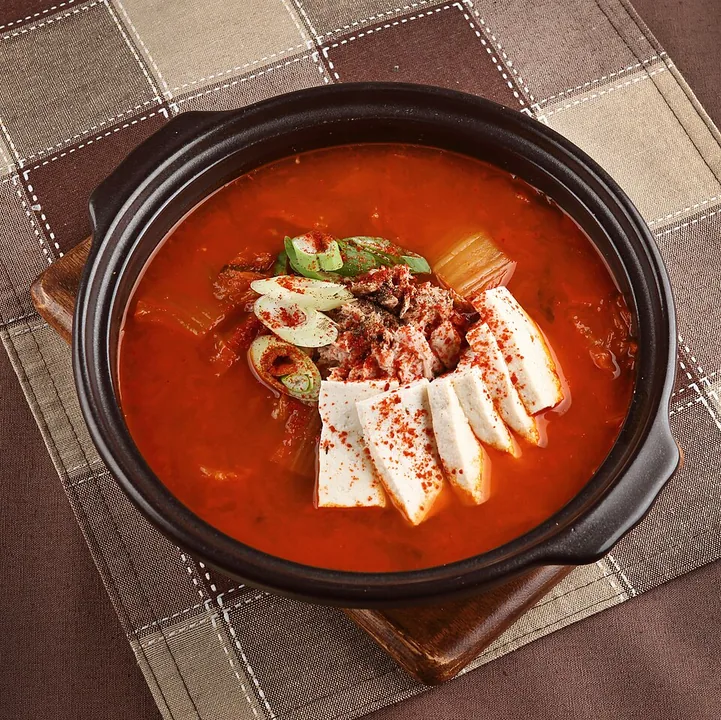 Red kimchi-jjigae stew with tofu, pork, kimchi and sliced green onion in a pot
