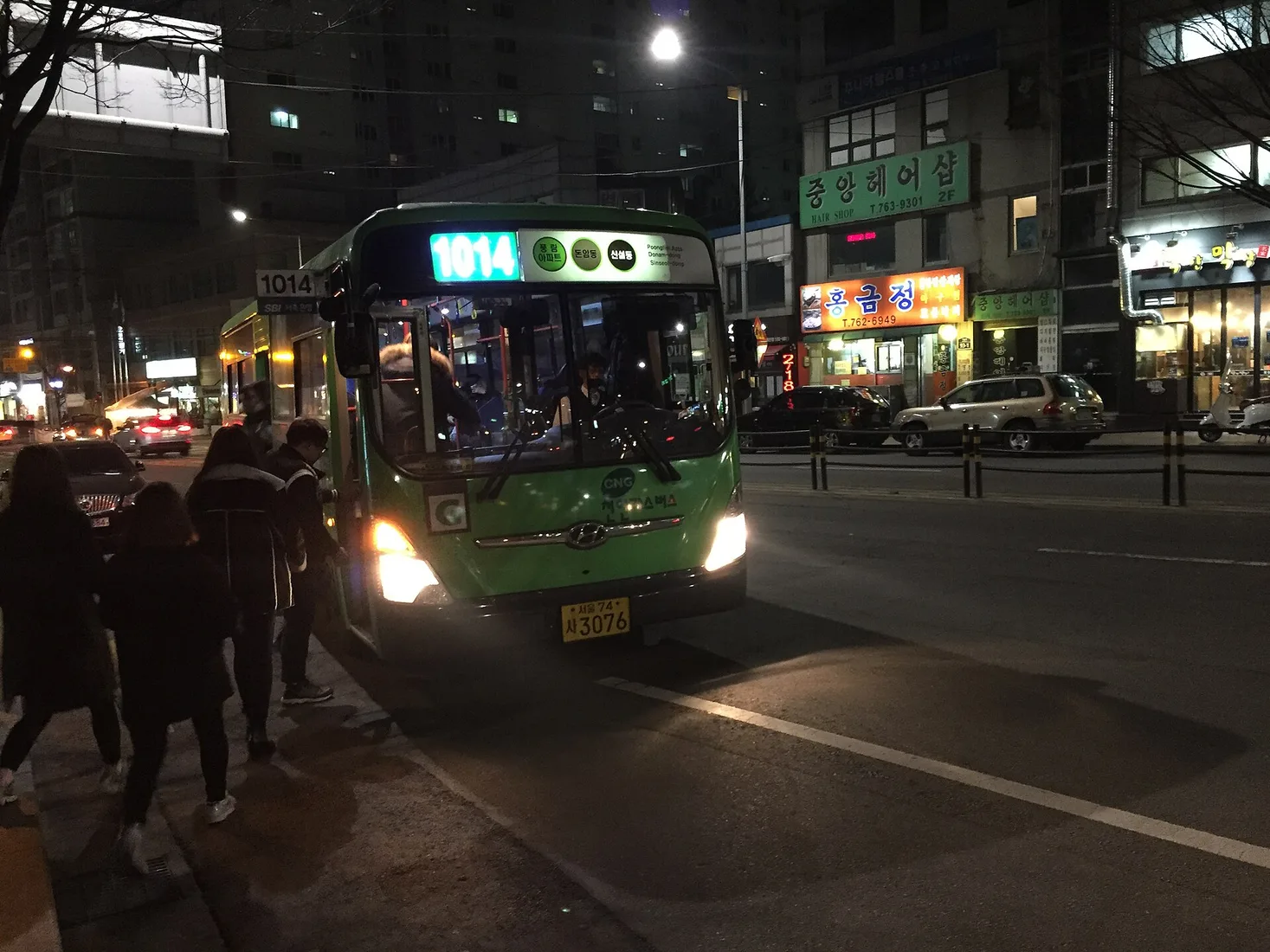 A green Seoul city bus operating on a lit street at night