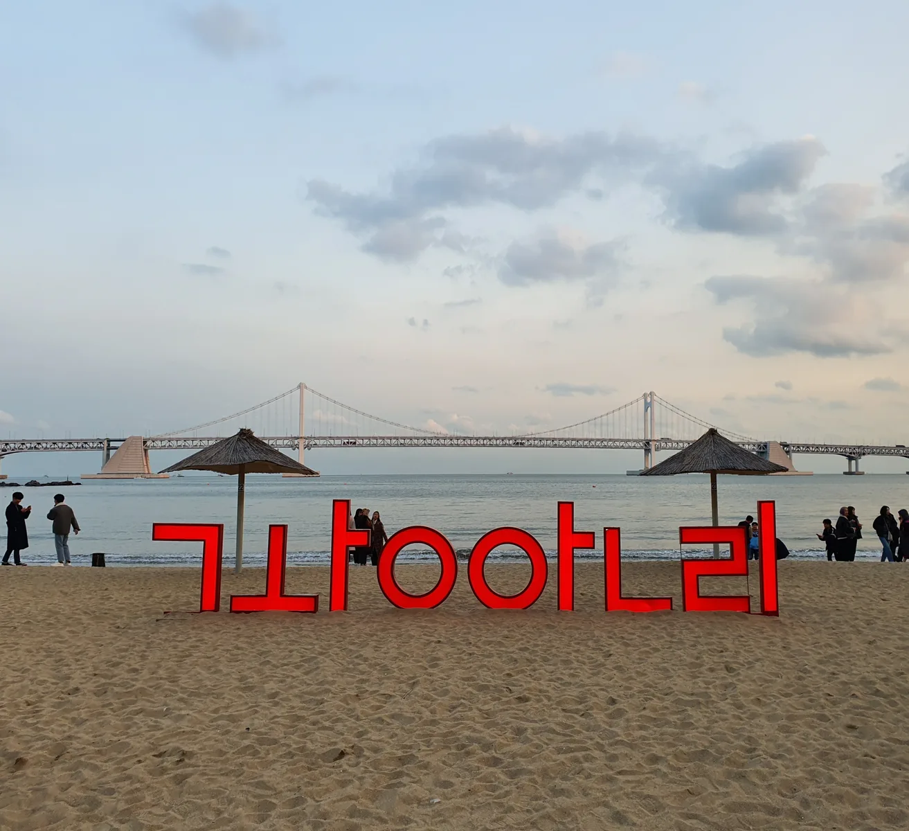 The red Gwangalli sign on the sandy beach with Gwangan Bridge spanning the water behind it