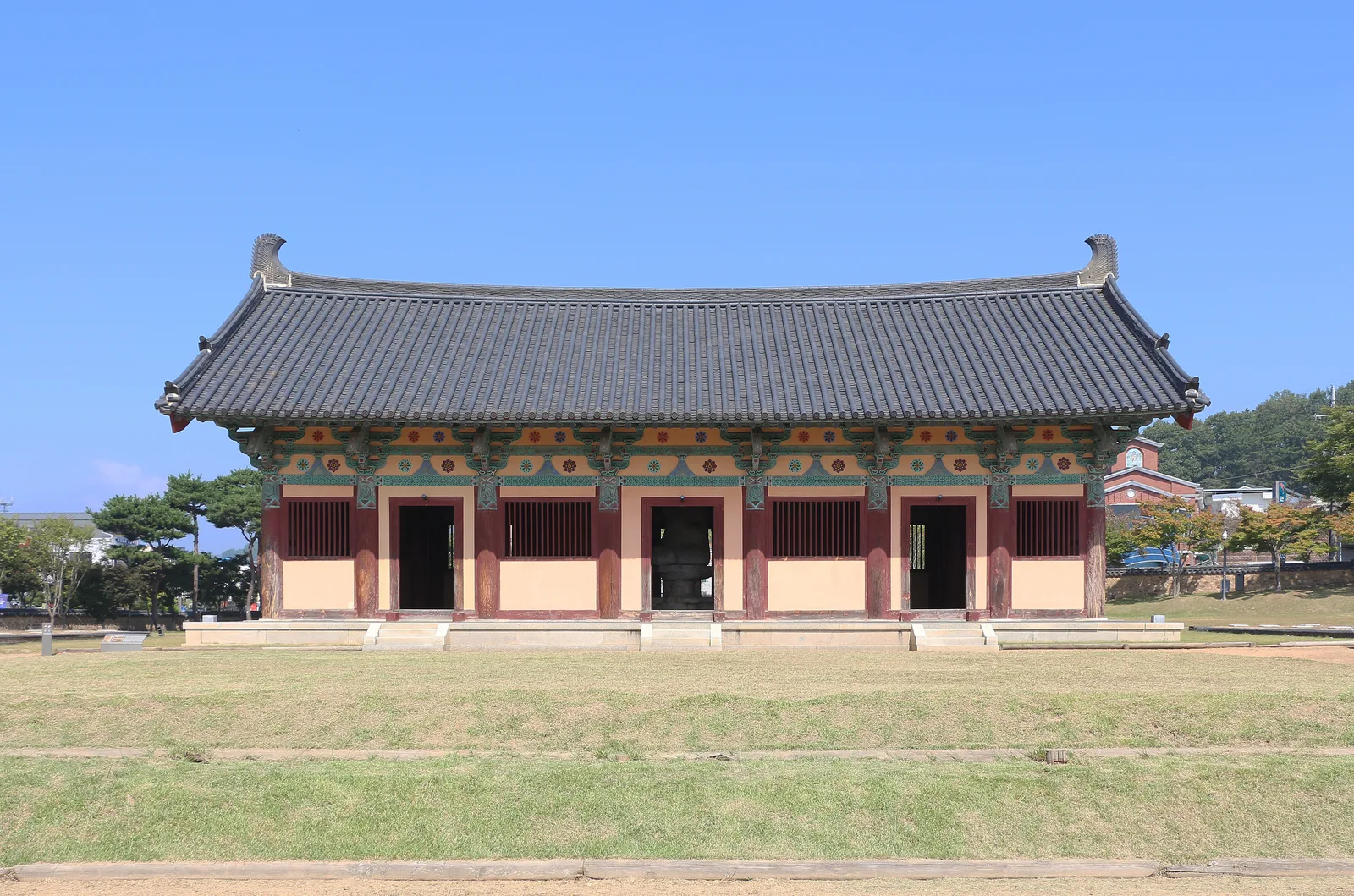 The tiled protection hall containing Jeongnimsa's stone seated Buddha, viewed across the temple-site lawn in Buyeo