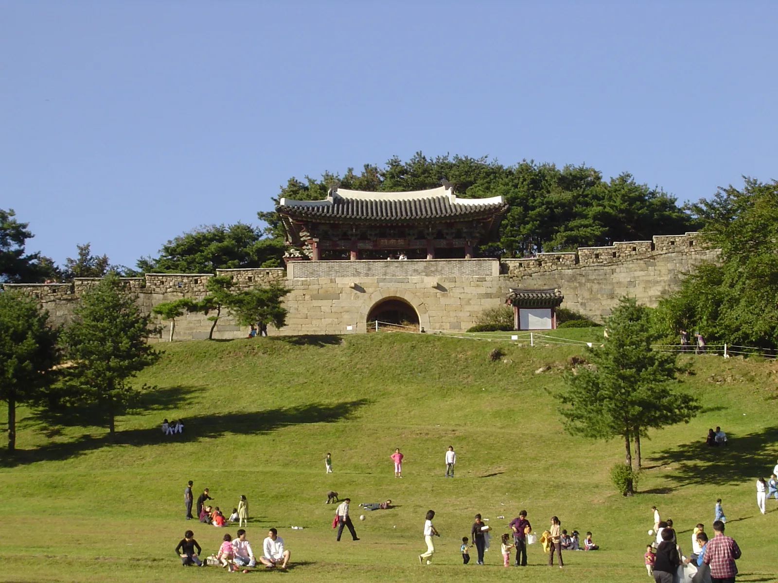 Visitors crossing the grassy grounds below a stone gate and wooded walls at Sangdangsanseong Fortress