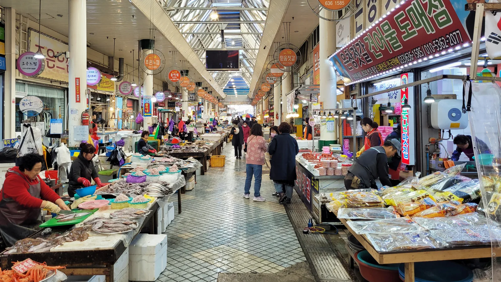 A covered seafood aisle with fish counters and shoppers inside Sokcho Tourist and Fishery Market