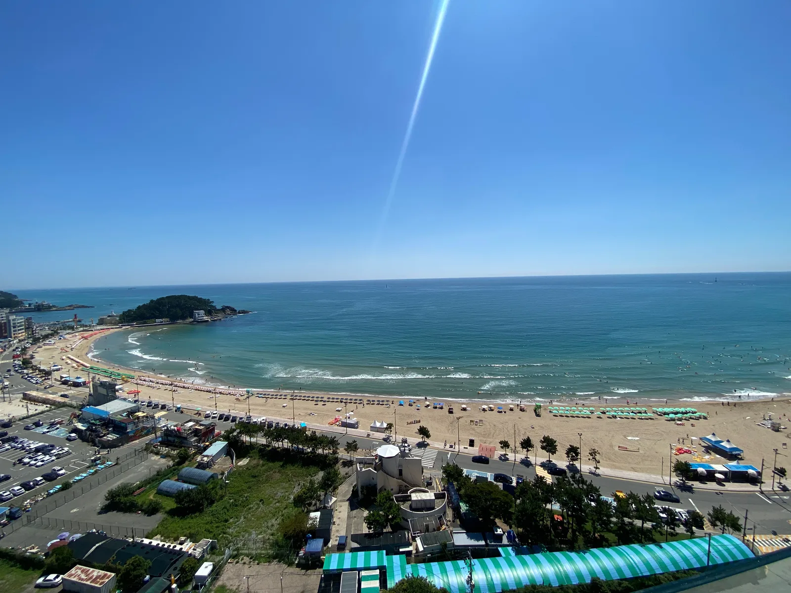 An elevated summer view over Songjeong Beach's curved sandy shoreline, water, umbrellas and waterfront road
