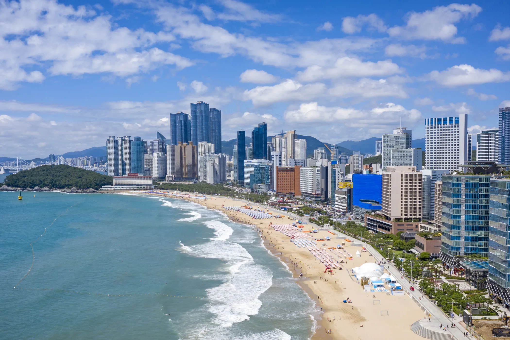 Aerial view east along the full sandy curve of Haeundae Beach toward the high-rise waterfront skyline