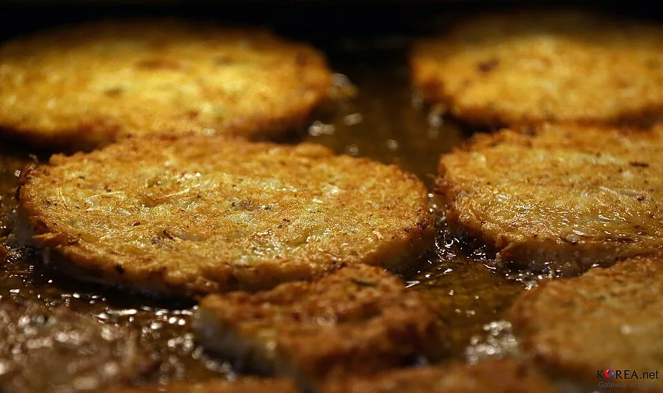 Round bindaetteok mung-bean pancakes frying in oil at Gwangjang Market