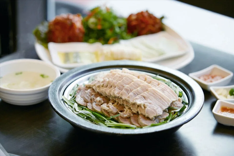 Sliced bossam pork arranged over vegetables with kimchi and sauces around the plate