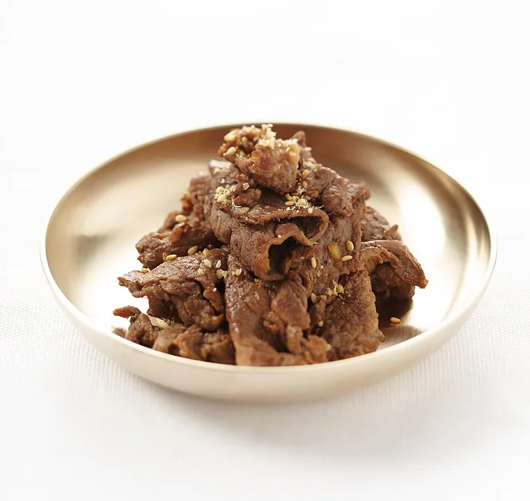 Cooked bulgogi beef served on a brass plate with sesame seeds on top