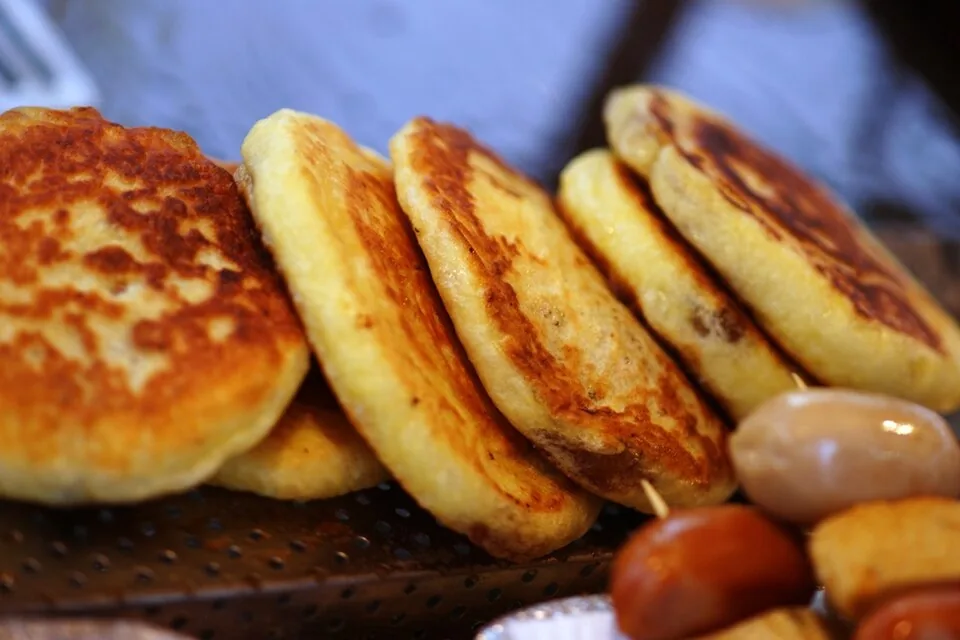 Freshly fried round hotteok pancakes served beside nuts on a wooden table