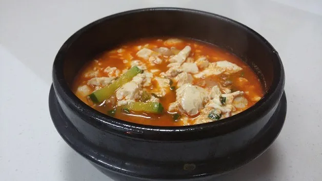 Soft tofu pieces and vegetables in a bubbling red bowl of sundubu-jjigae