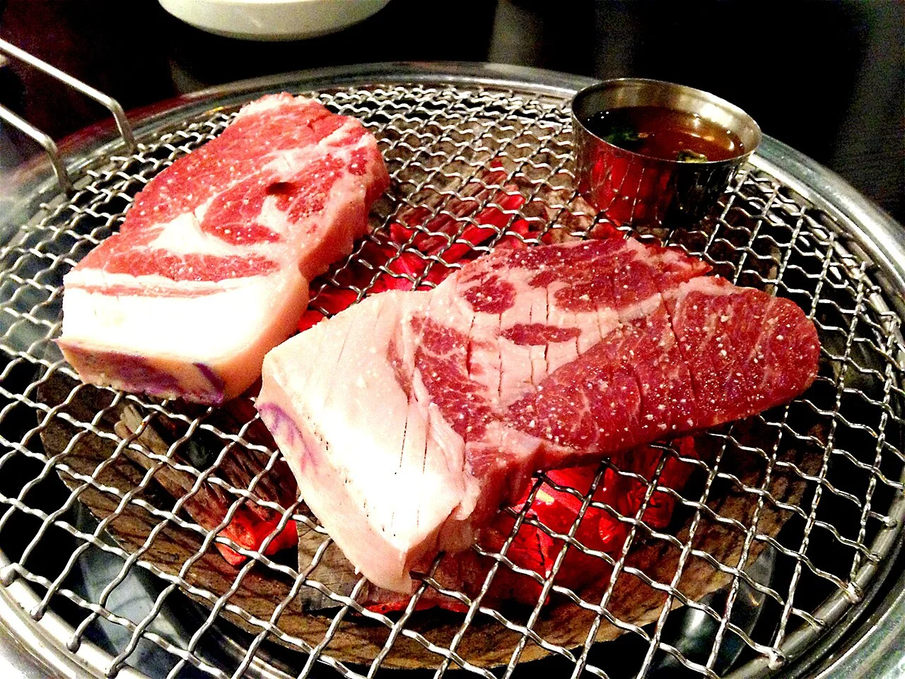 Thick slices of Jeju black pork cooking over charcoal on a round grill