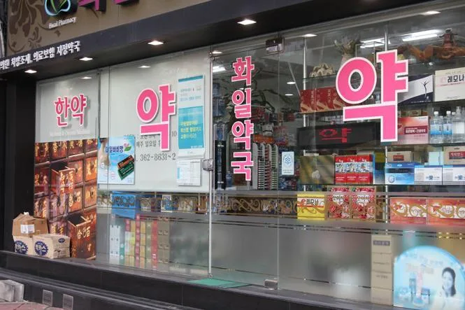 A Korean pharmacy storefront with the large red Hangul character for medicine