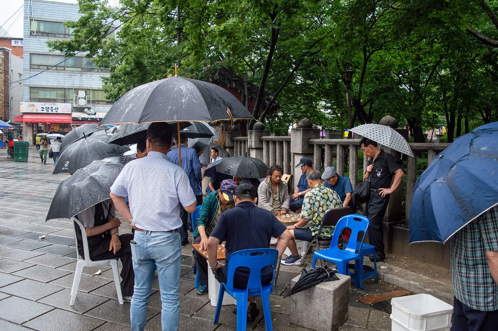 People sheltering under umbrellas beside Tapgol Park during rain in Seoul