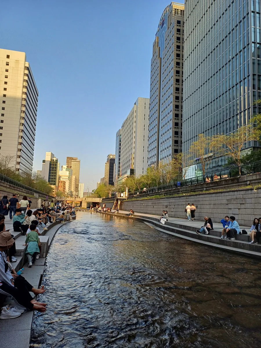 Pedestrians sitting and walking beside the shallow Cheonggyecheon stream between central Seoul office towers