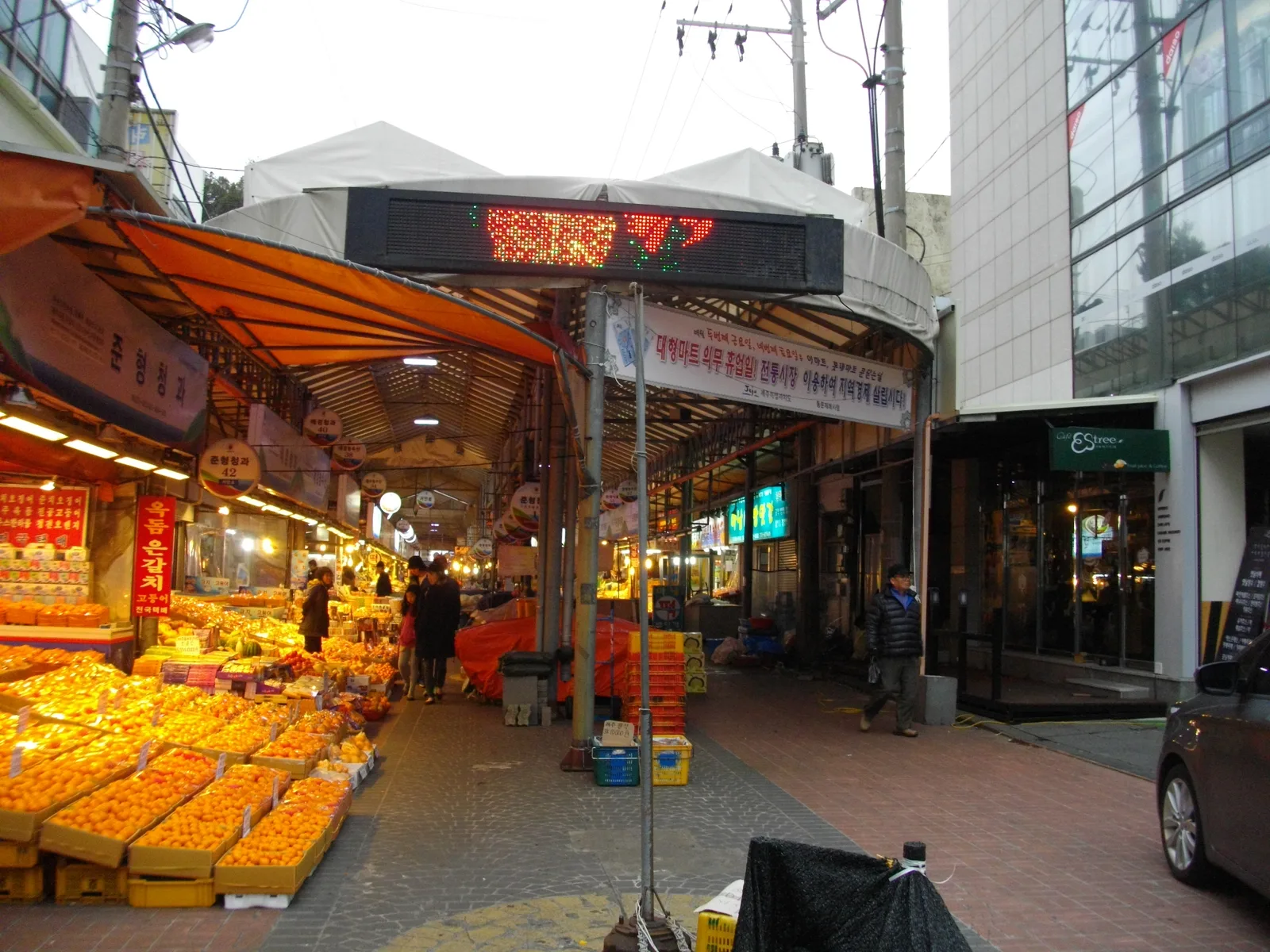 A covered entrance lane at Jeju Dongmun Market with bright fruit displays and Korean shop signs