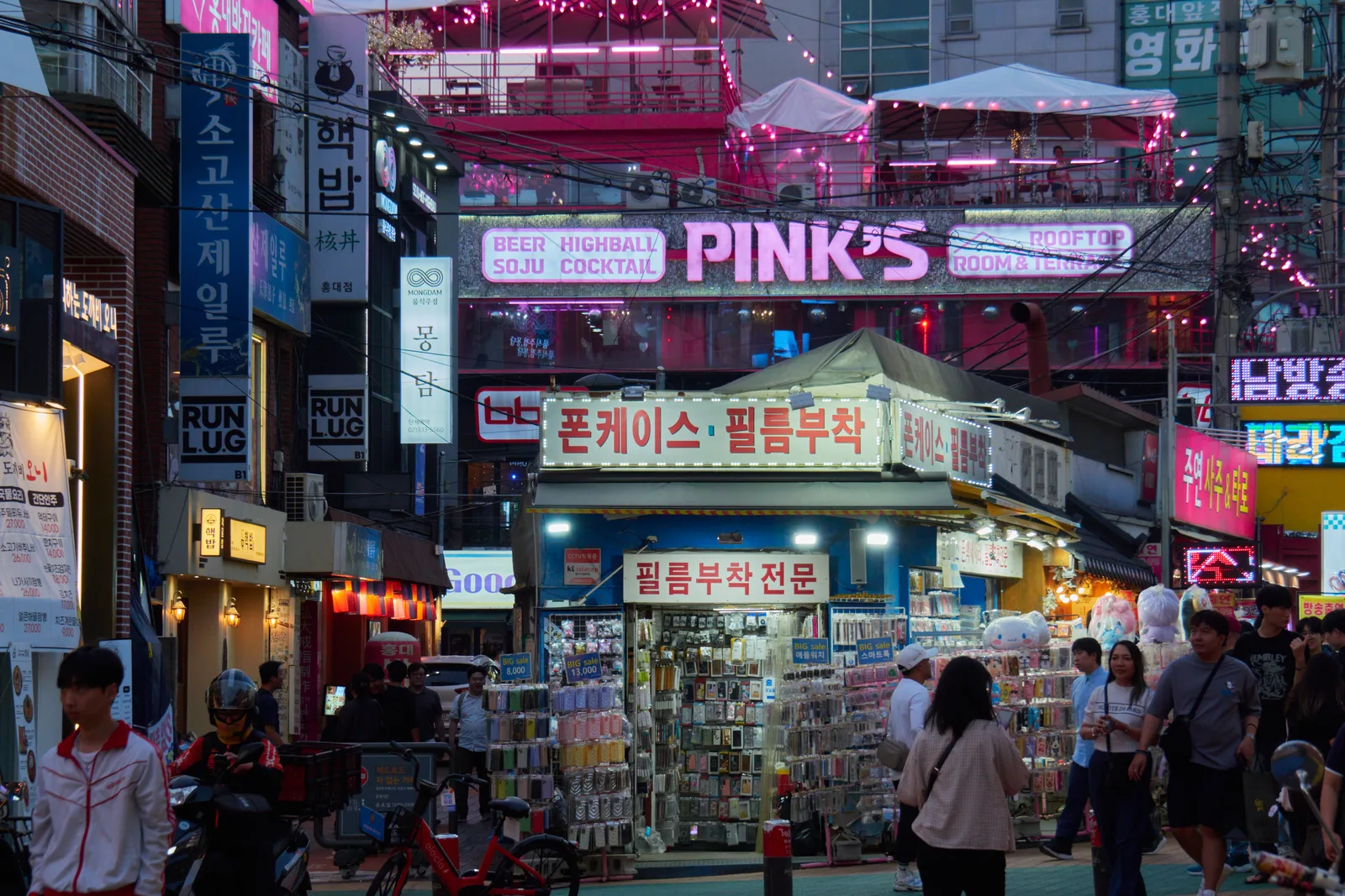 Pedestrians, accessory stalls and neon storefronts on a busy Hongdae street at night