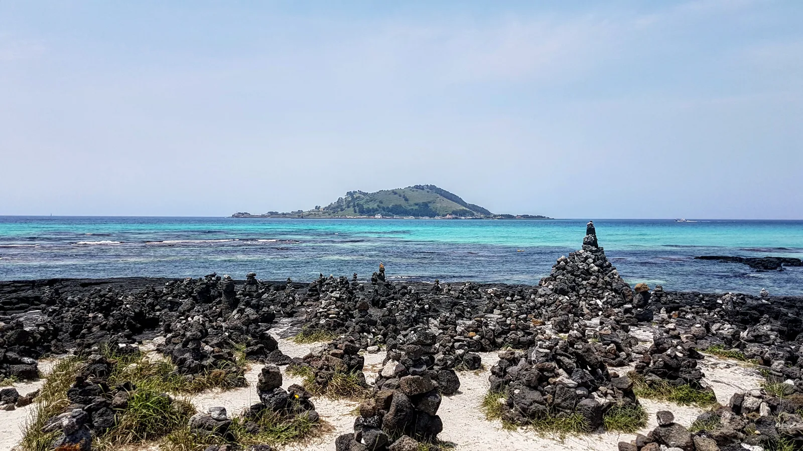 Dark basalt rocks, clear turquoise water and Biyangdo Island across the real shoreline at Hyeopjae Beach