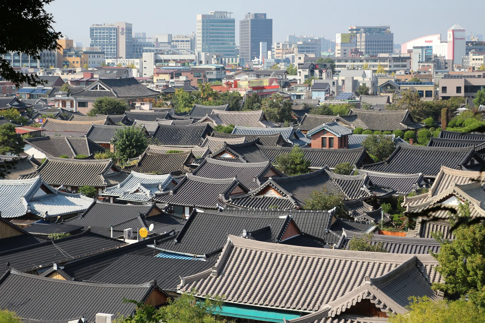 A broad view across the tiled hanok roofs of Jeonju Hanok Village with the modern city skyline beyond